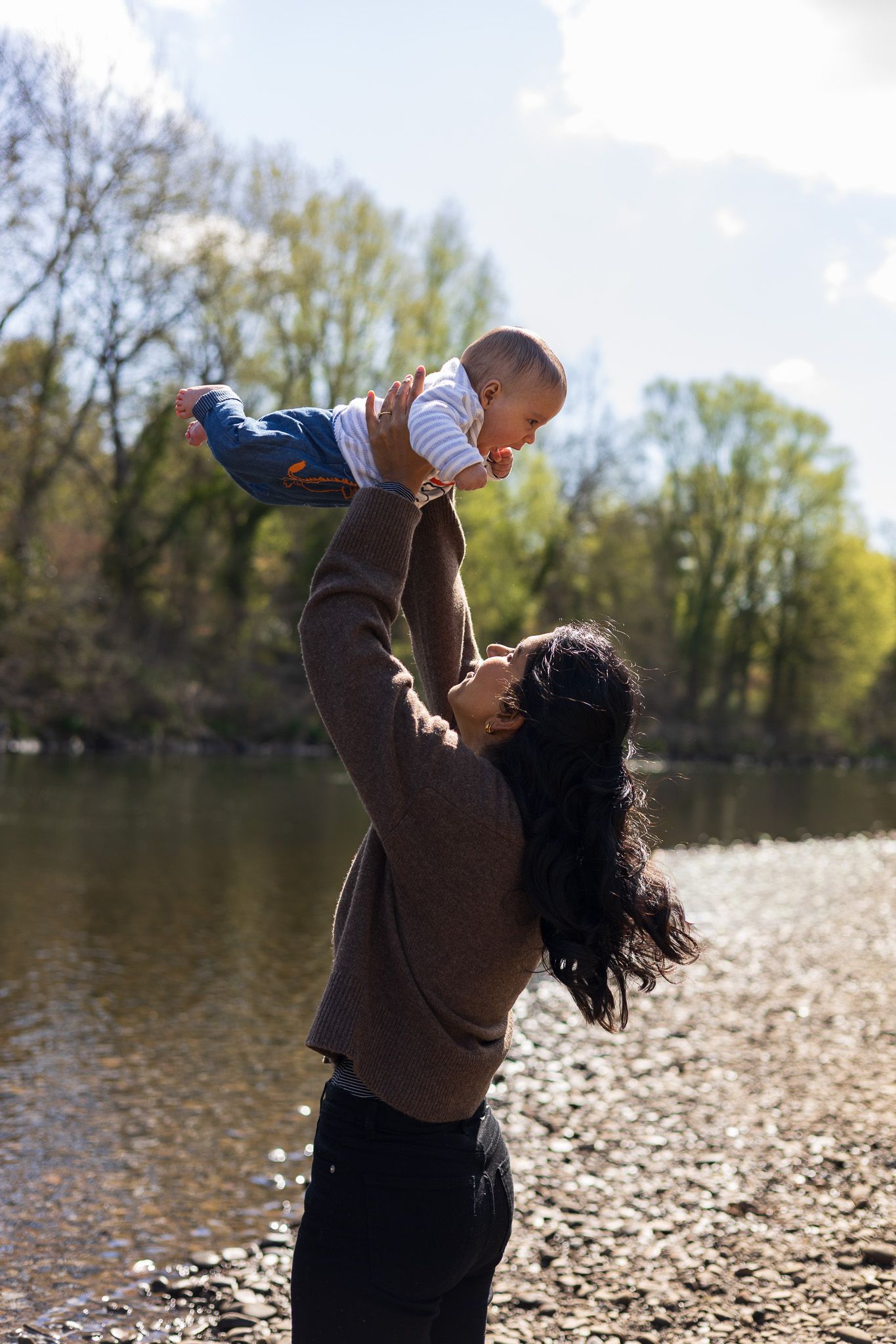Mother lifting her toddler up joyfully by the riverside