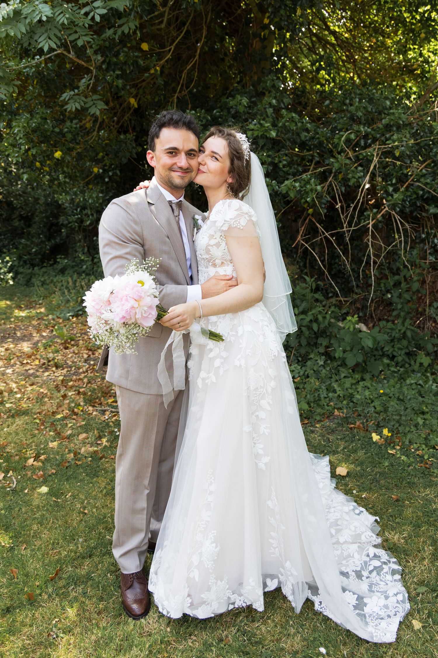 Bride and groom posing together in a garden, bride holding her bouquet