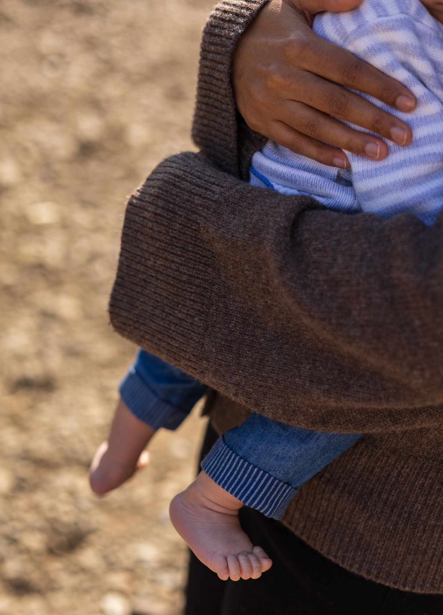 Close-up of a toddler's hand resting on his mother's shoulder by the riverside