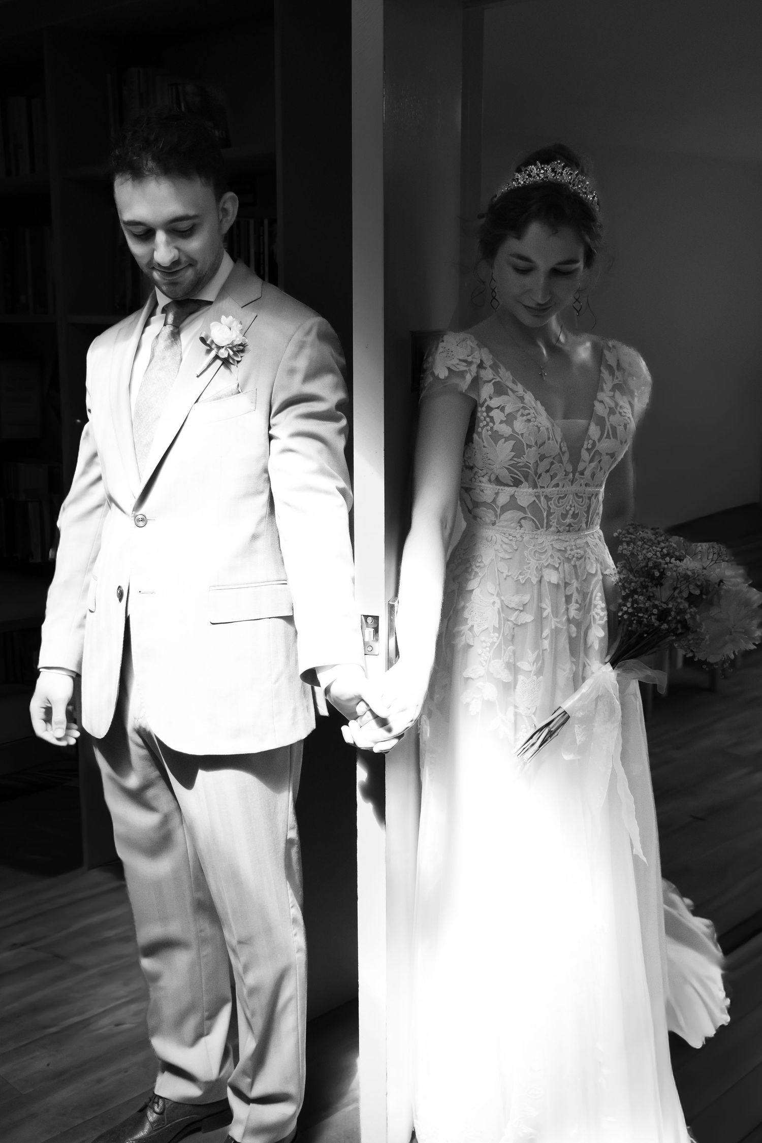 Black and white photo of groom leading bride out through a doorway