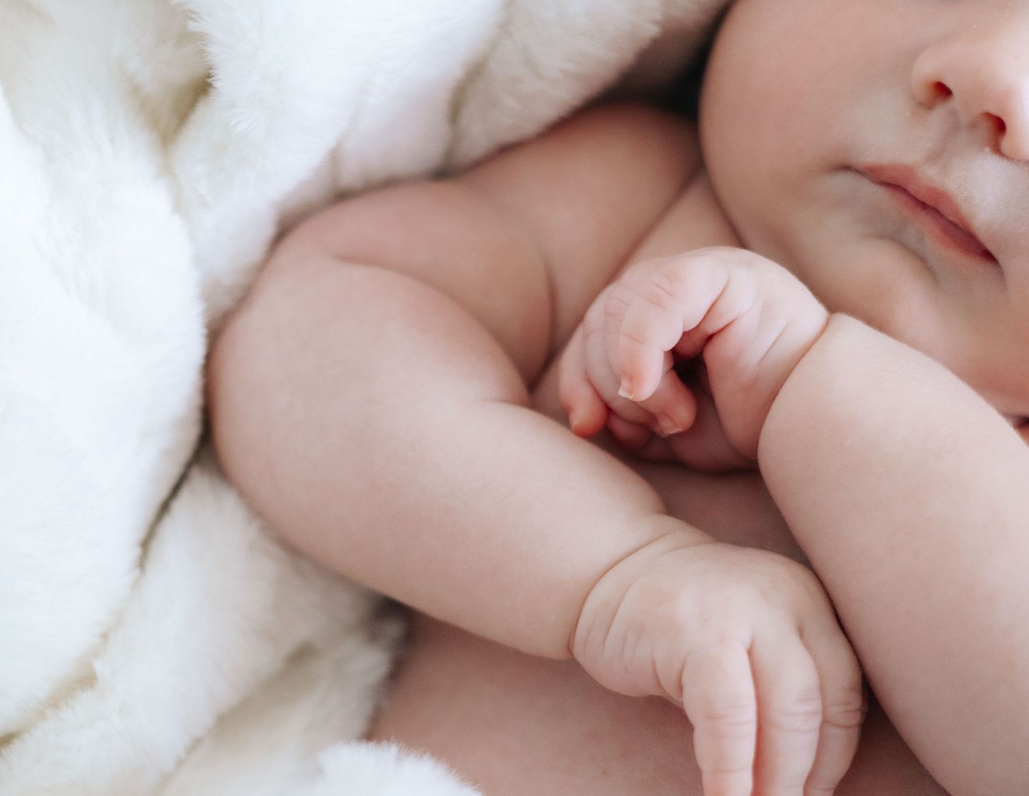 Close-up of a sleeping newborn baby wrapped in a soft white blanket