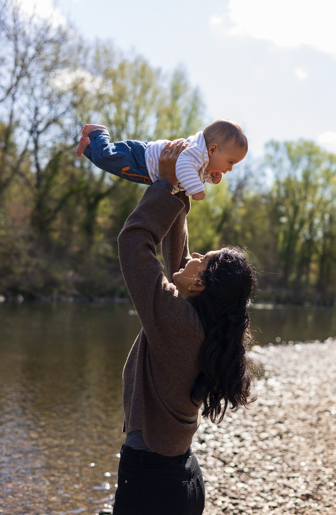 Mother lifting her toddler up joyfully by the riverside