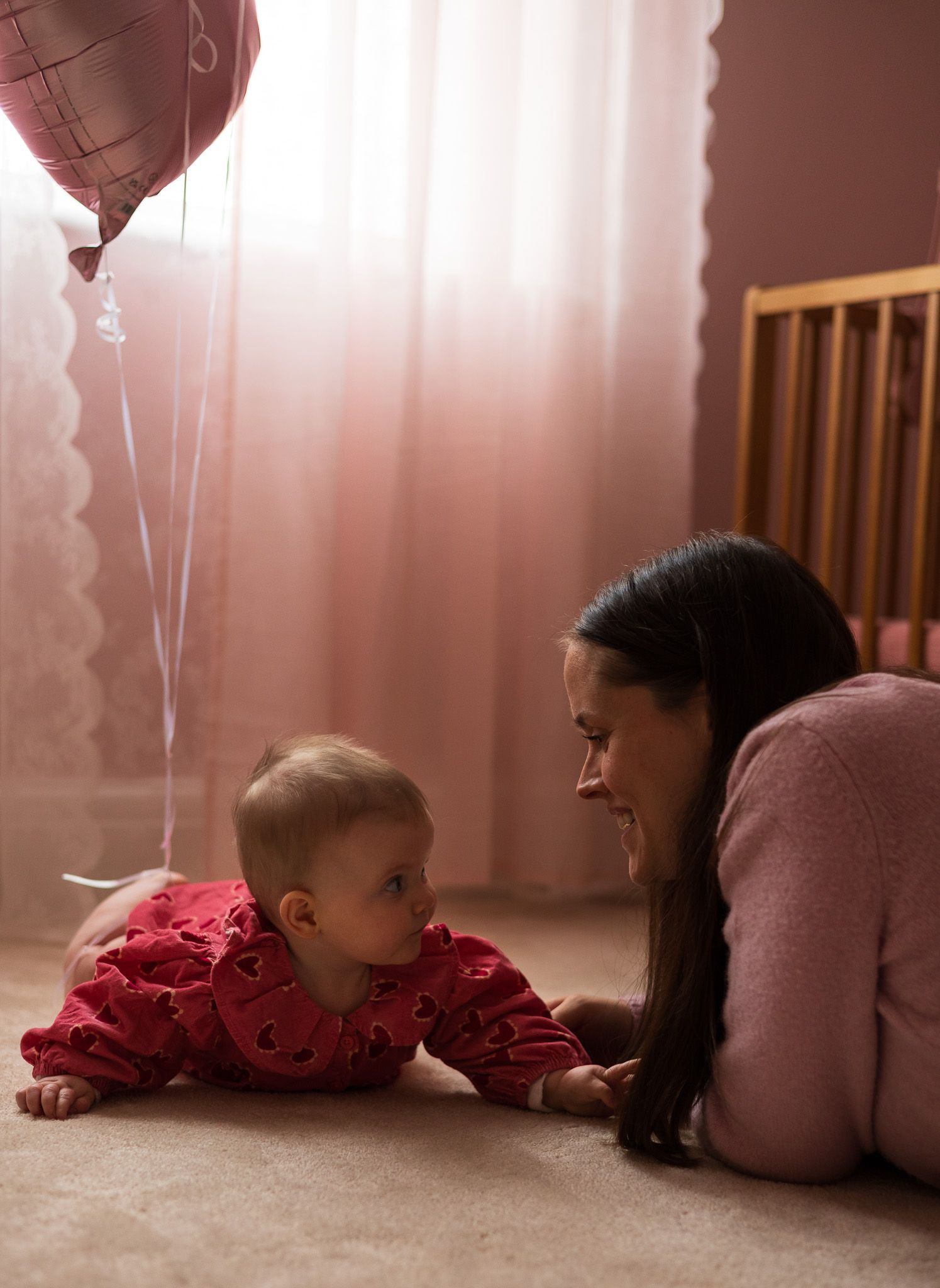 Mother lying on the floor with her baby beside a heart balloon in the nursery