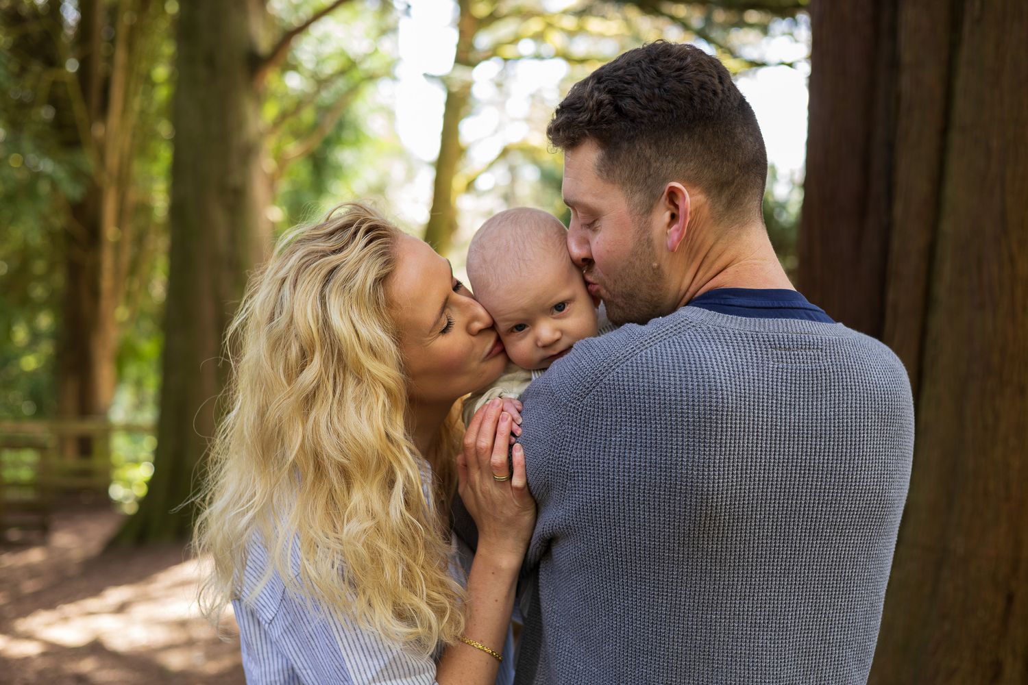 Parents kissing their baby together in the woods