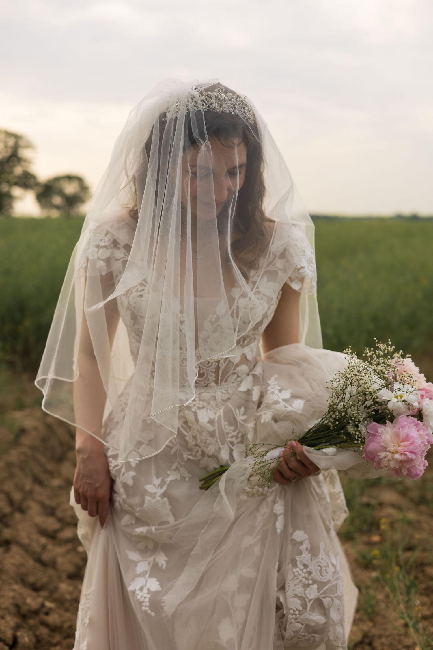 Bride in flowing veil holding her bouquet, standing in a field