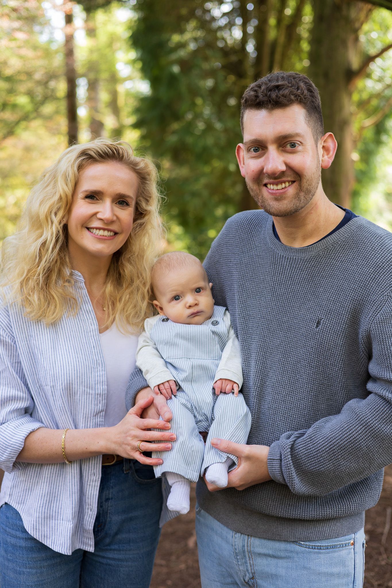 Family of three smiling together at the camera in the woods