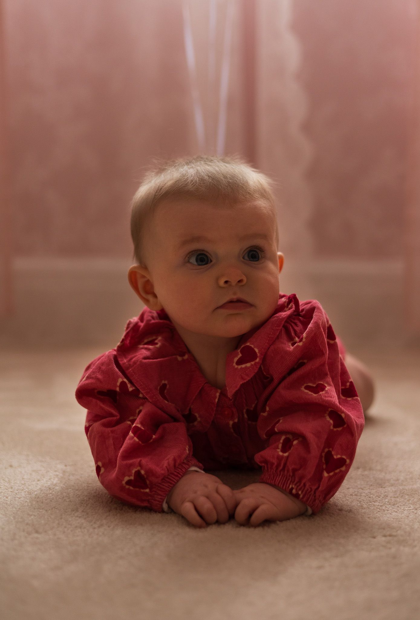 Baby in a red outfit sitting on a pink blanket