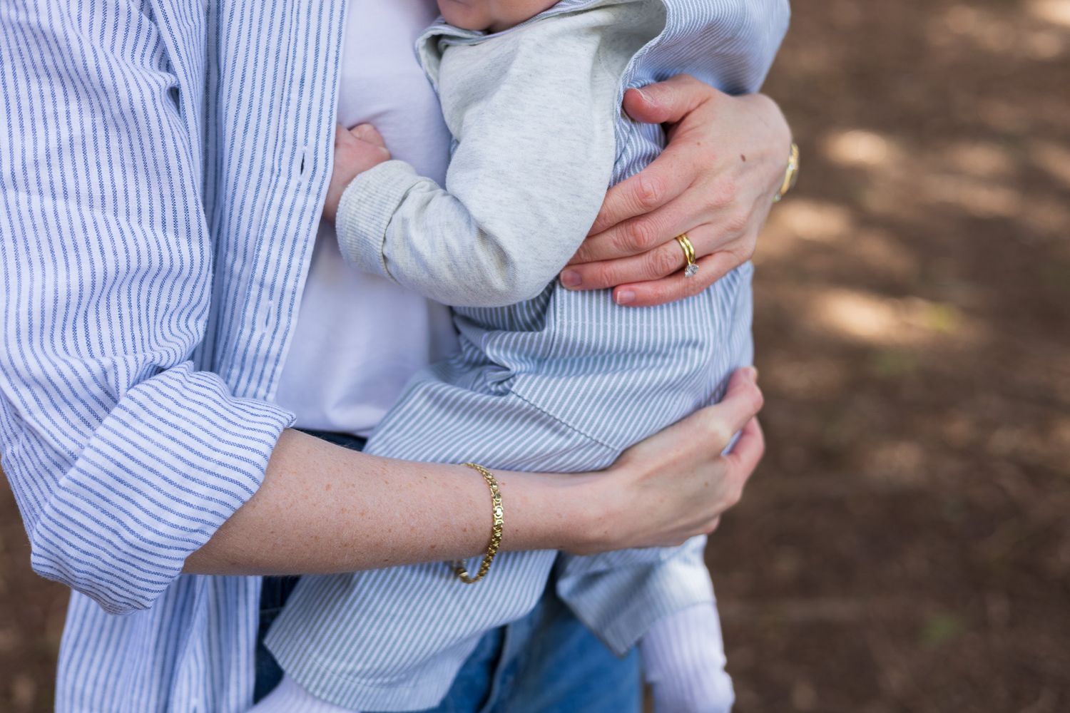 Close-up of parents' arms cradling their baby outdoors