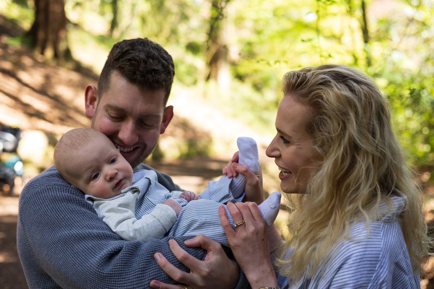 Parents smiling and holding their baby together in the woods