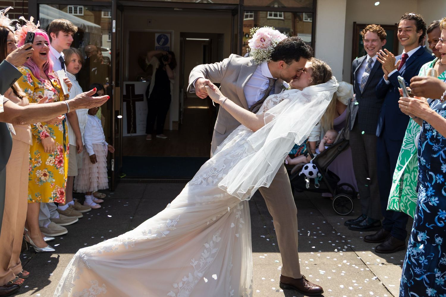 Groom dipping and kissing bride as guests throw confetti around them