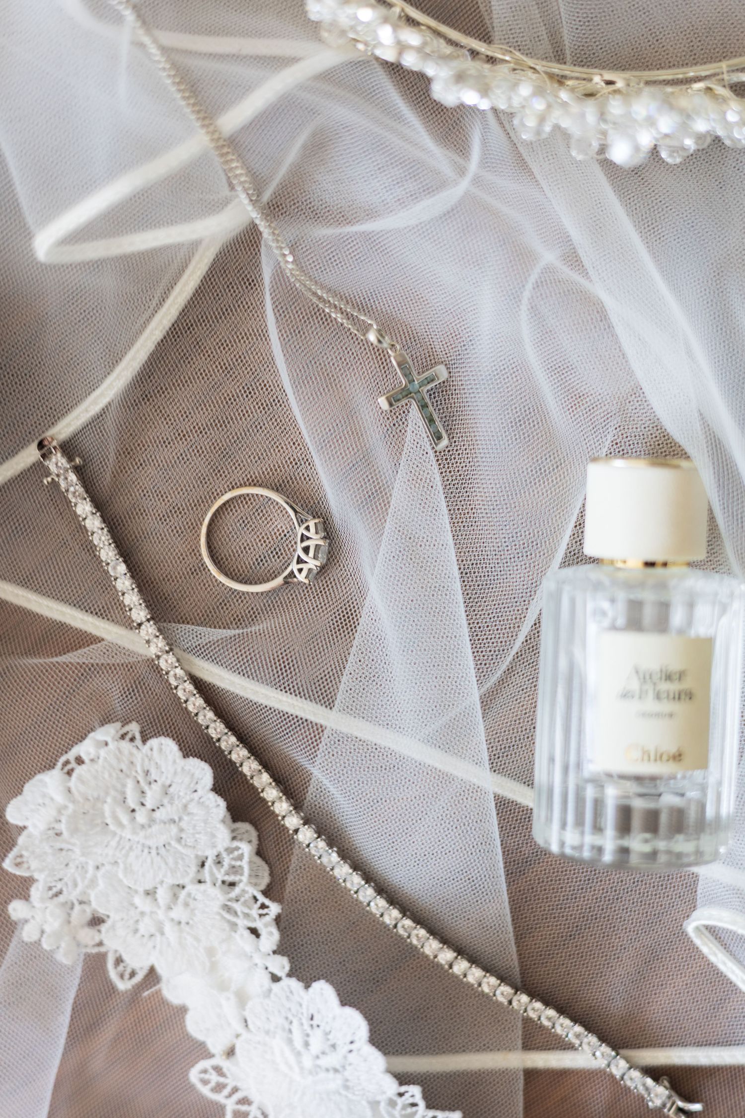 Flat lay of wedding day details including veil, perfume, and jewellery