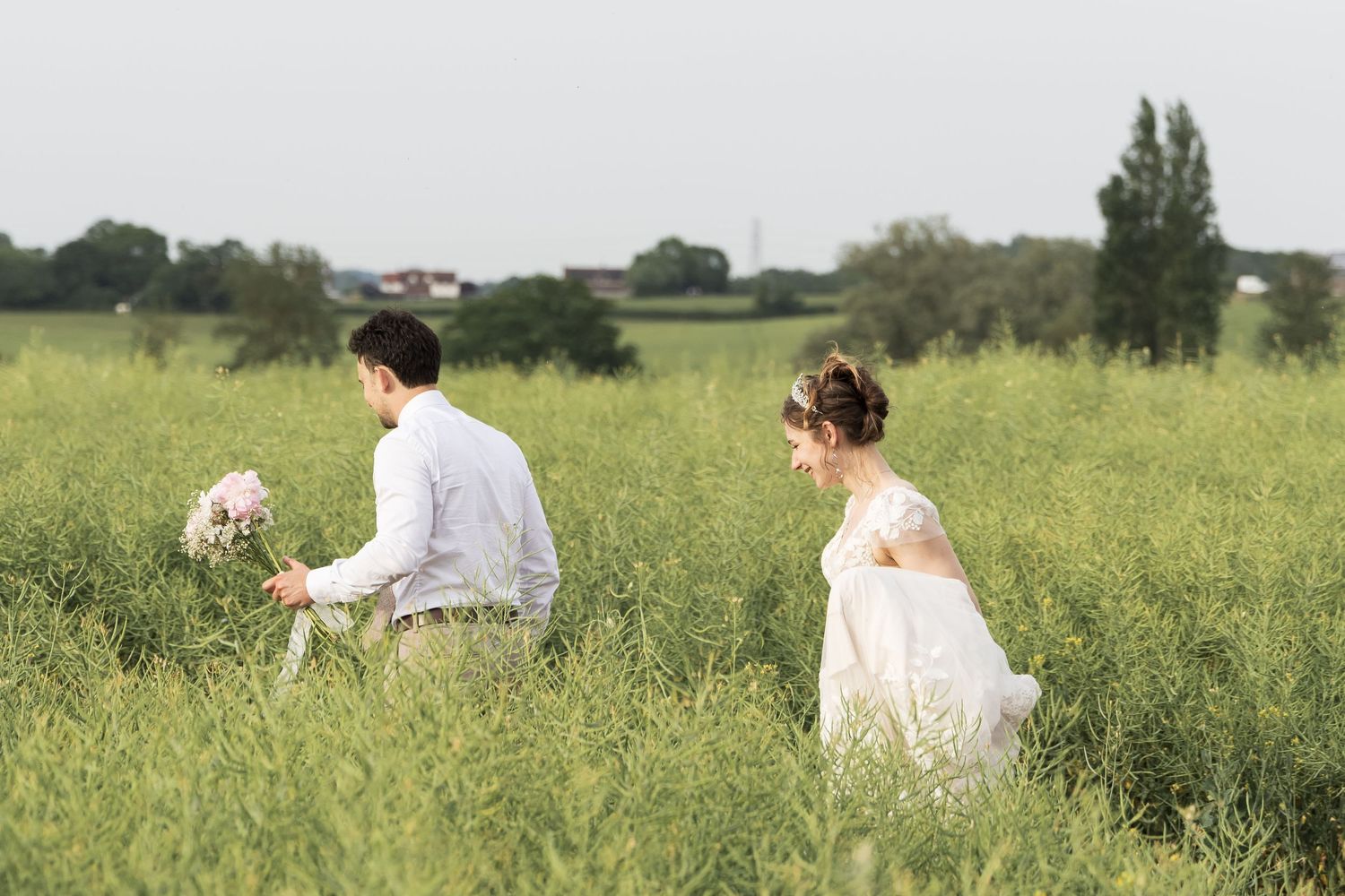 Bride and groom walking hand in hand through a green field