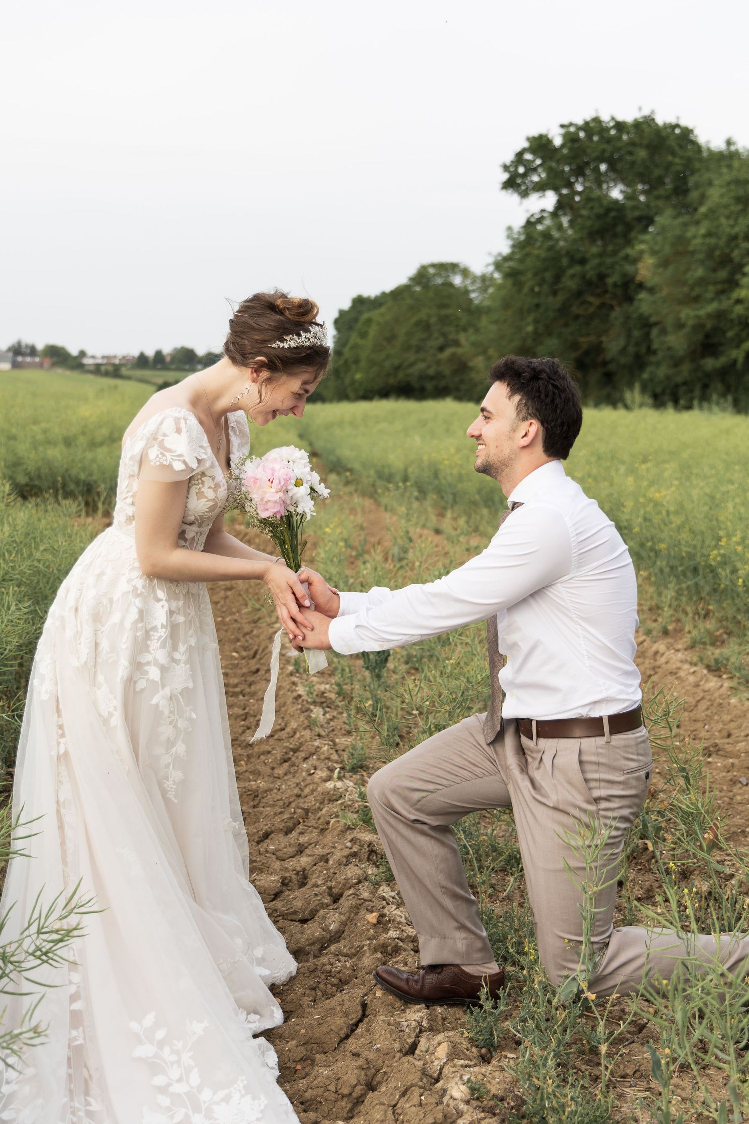 Groom kneeling and presenting flowers to his bride in a field