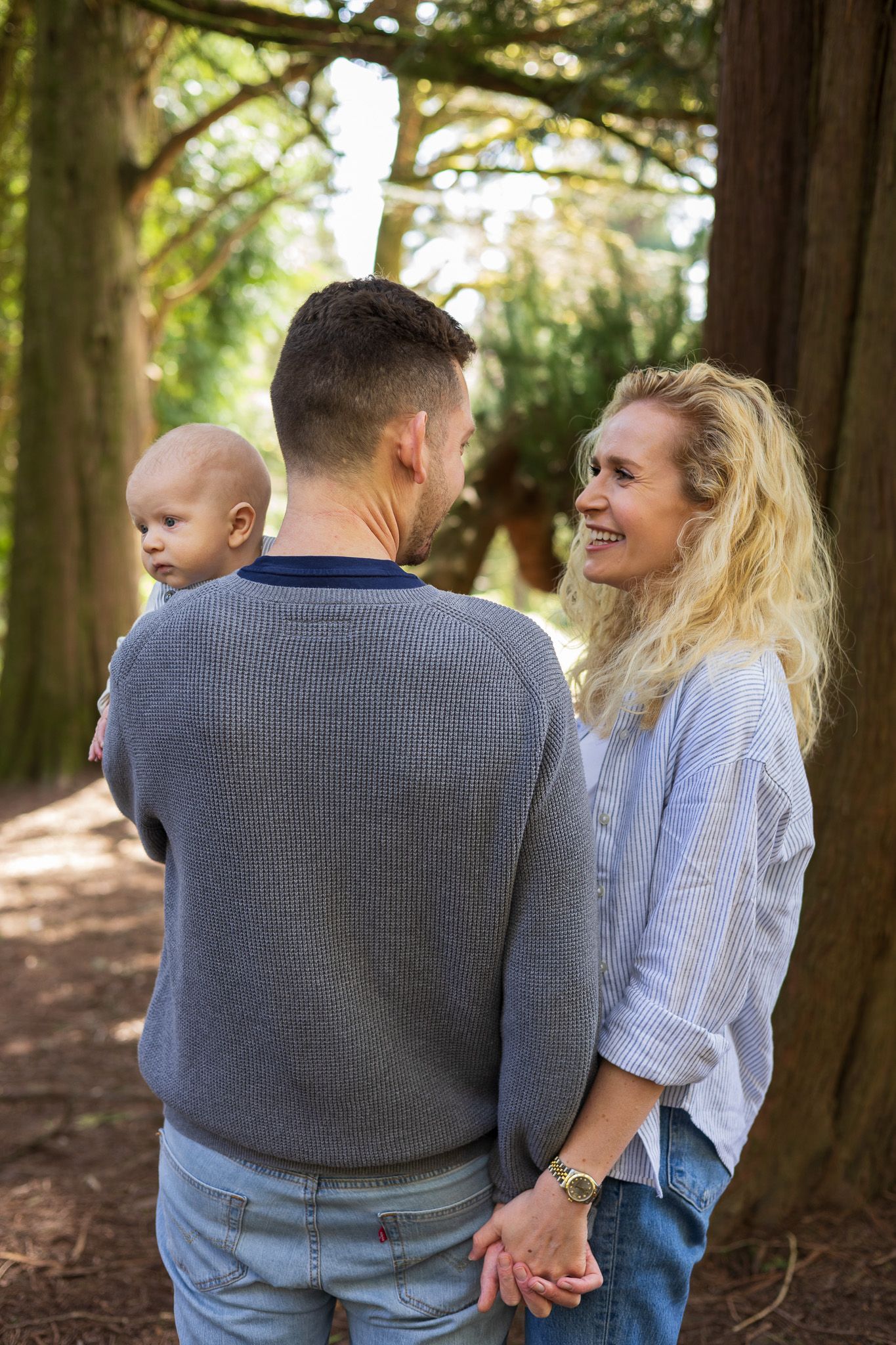 Father carrying toddler while walking with mother through a woodland path