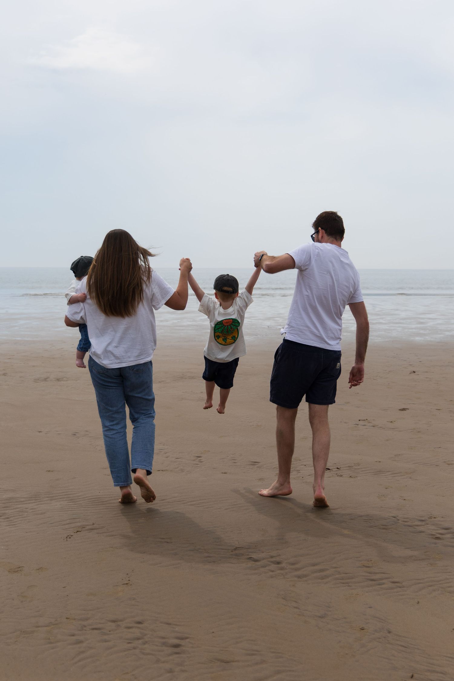 Family of three holding hands and walking along the beach