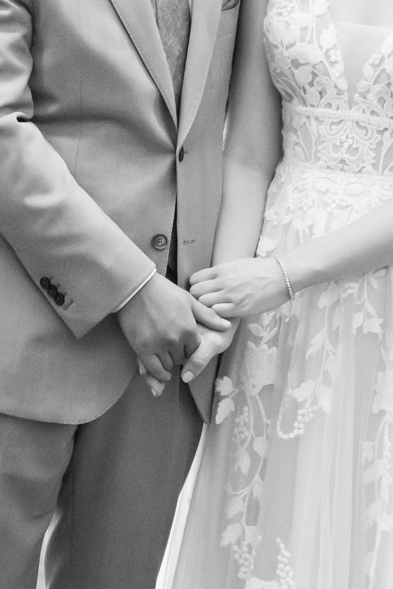 Black and white close-up of bride and groom holding hands during their ceremony