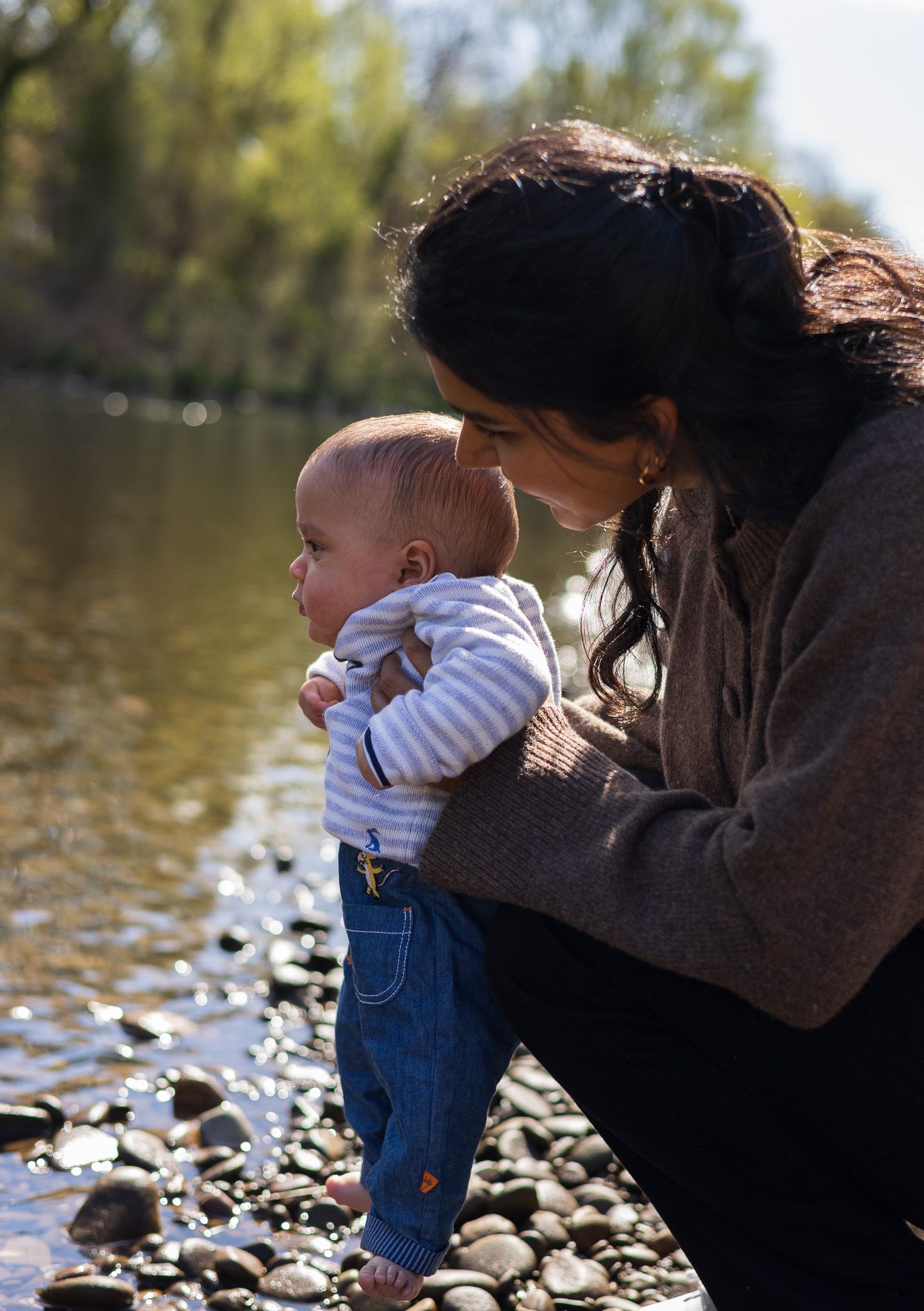 Mother crouching down to hold her toddler by the riverside