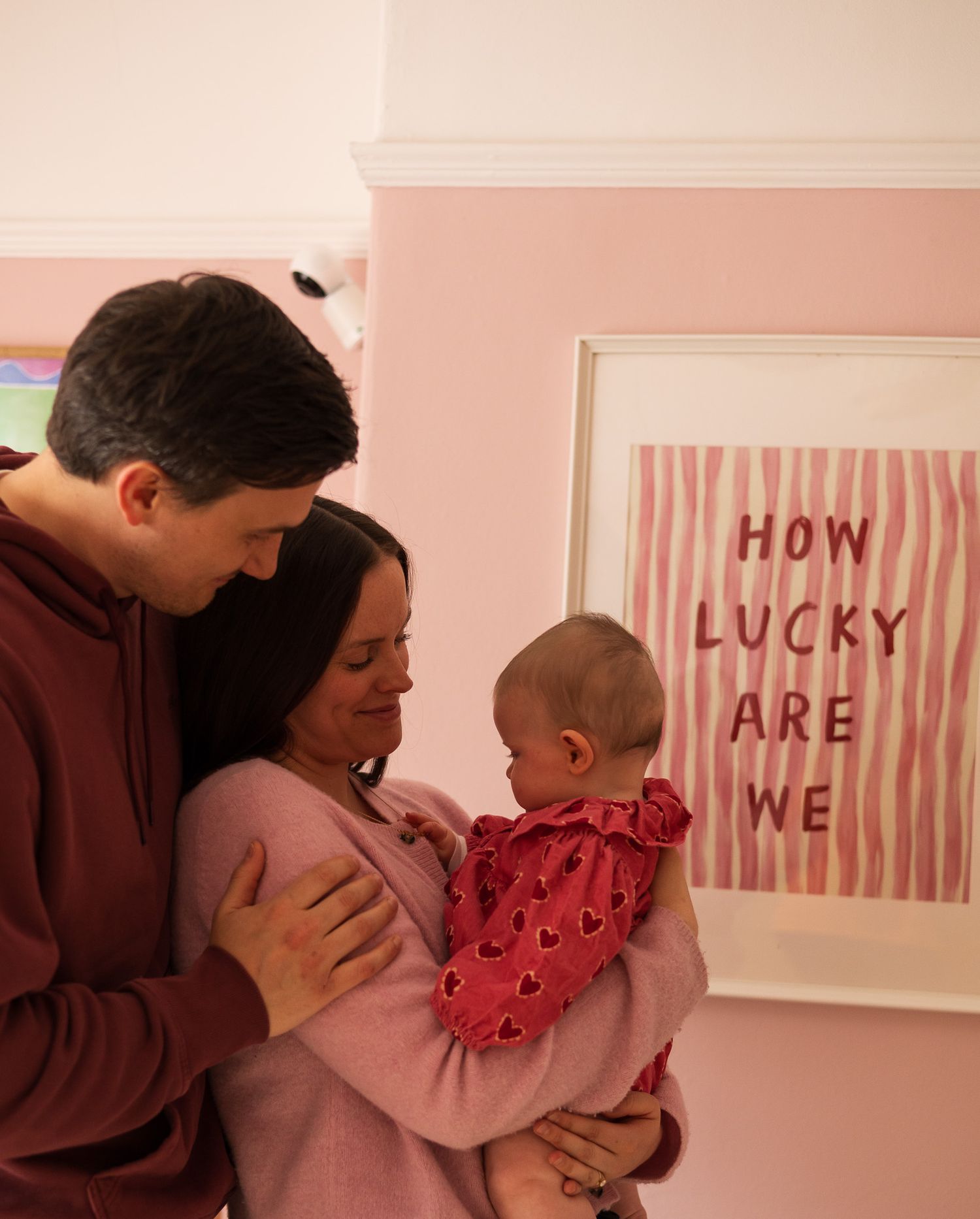 Parents holding their baby beside a 'How Lucky Are We' sign