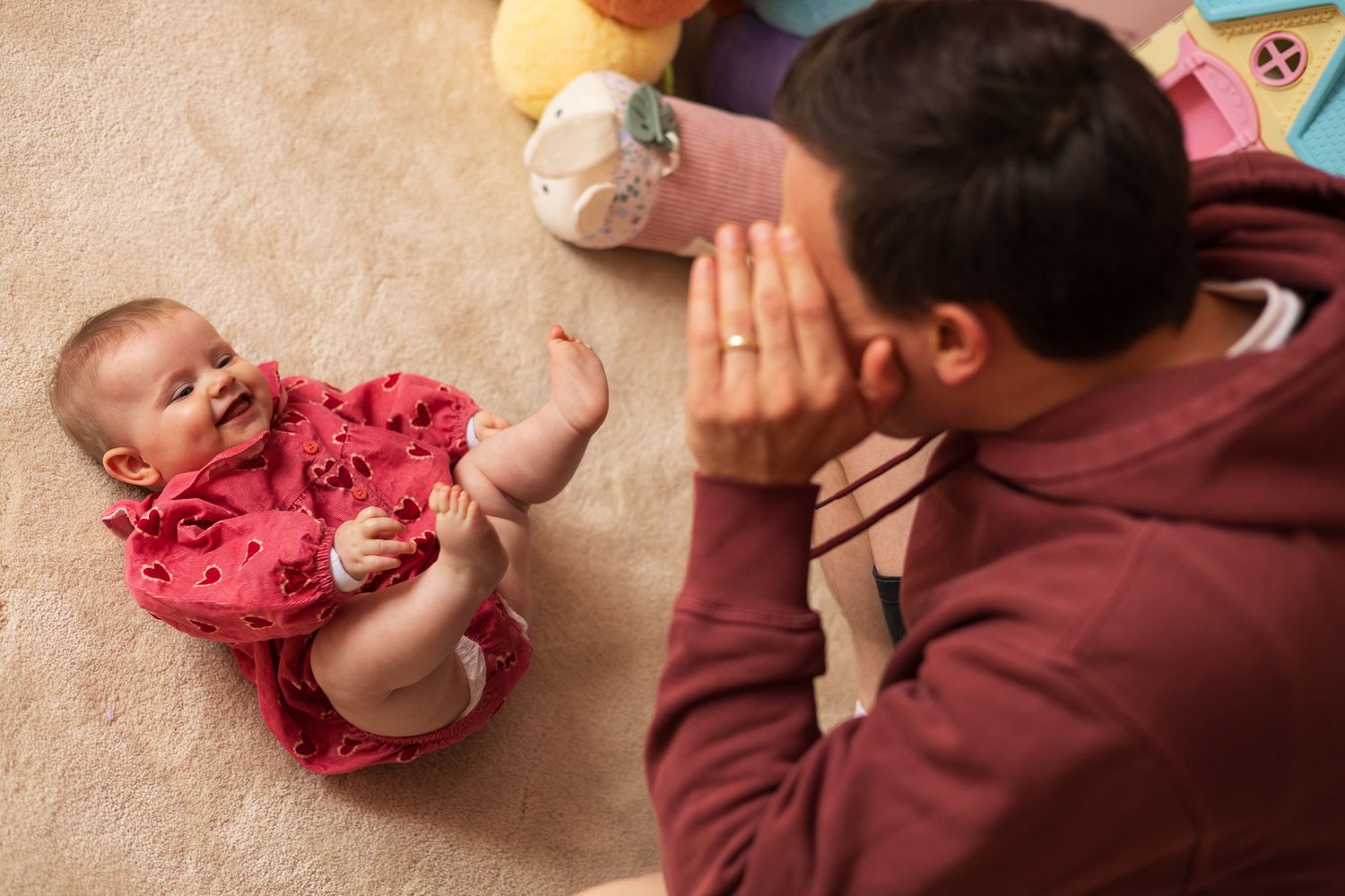 Father playing peekaboo with his baby on the nursery floor