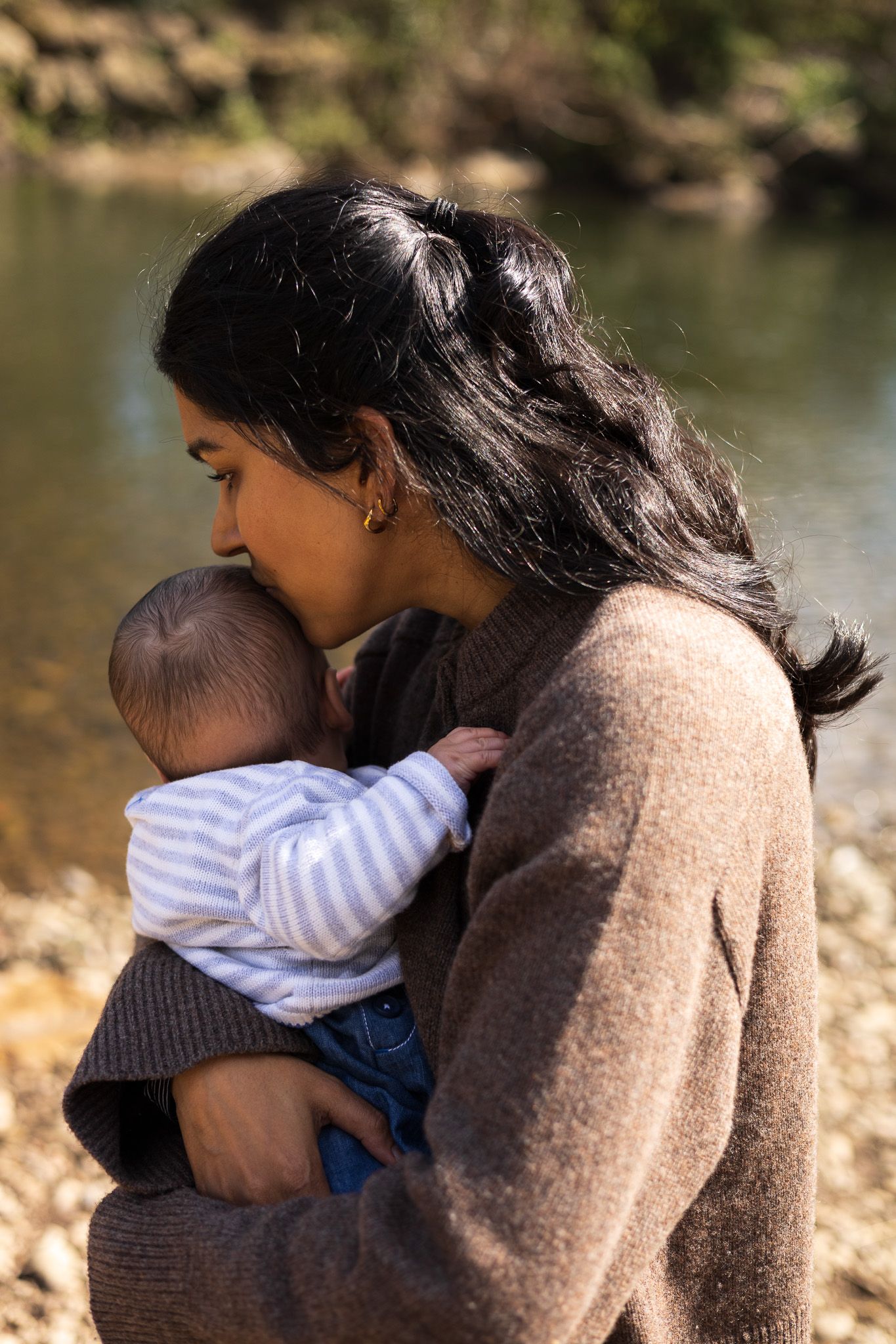 Mother kissing her baby's head while holding him by the riverside