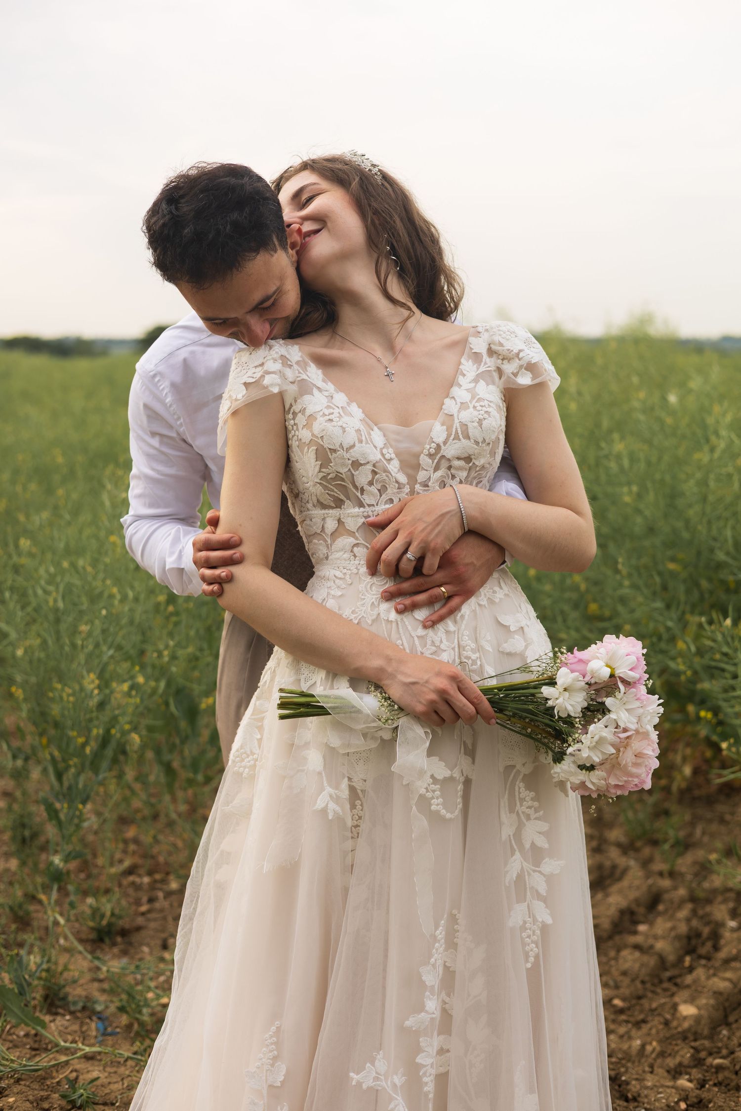 Groom embracing bride and holding bouquet together in a wildflower field