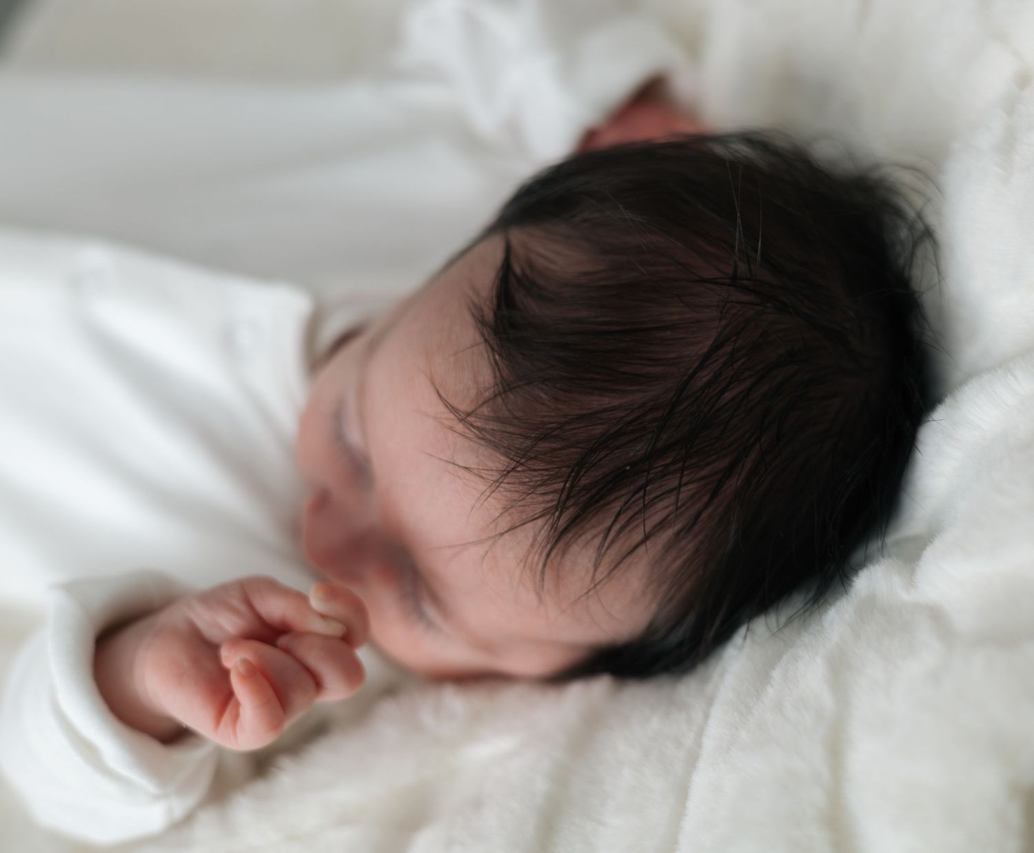 Sleeping newborn baby with dark hair wrapped in white blankets