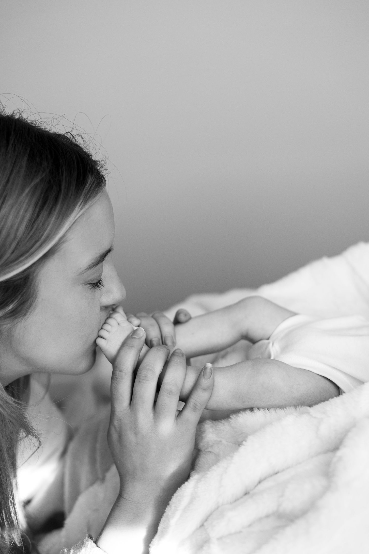 Black and white close-up of a mother kissing her baby's tiny hands