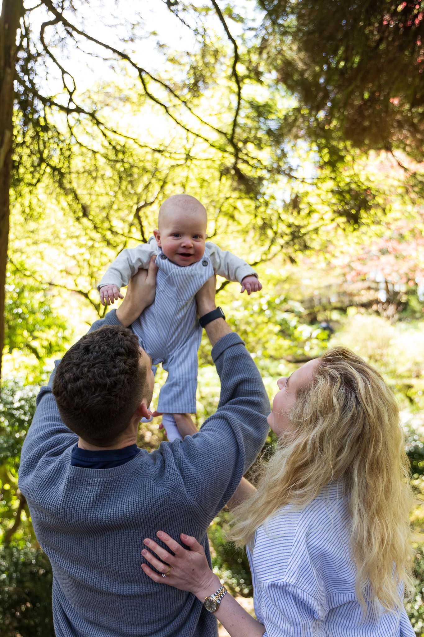 Father lifting his baby up high in the air among the trees