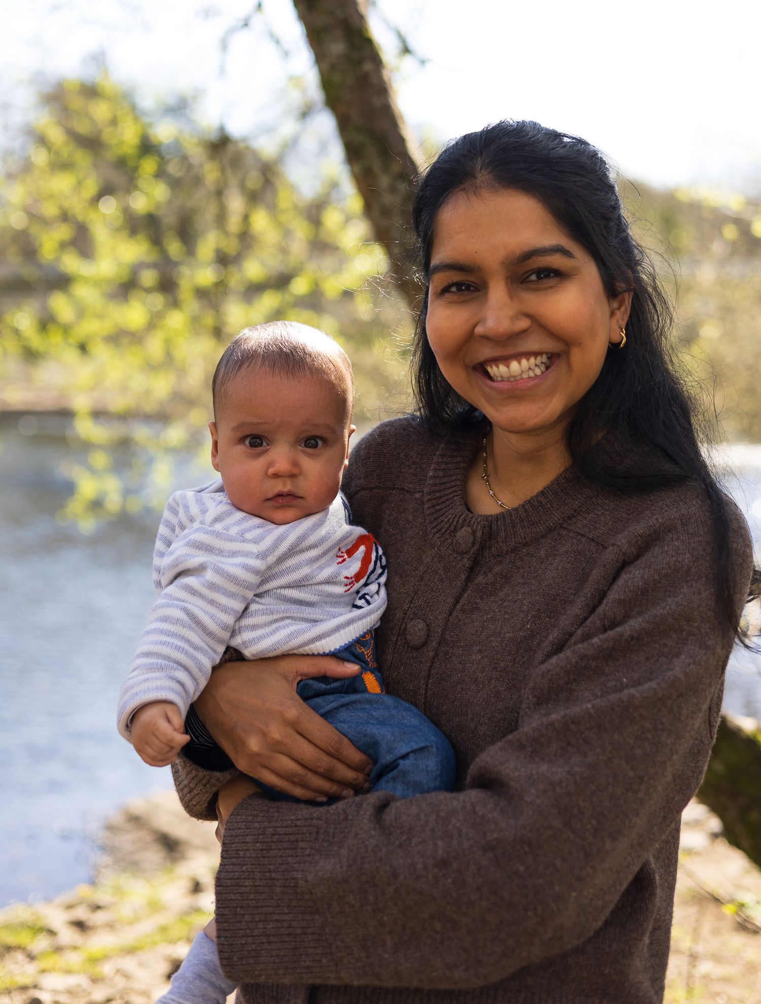 Mother holding her baby by the water during an autumn family photoshoot