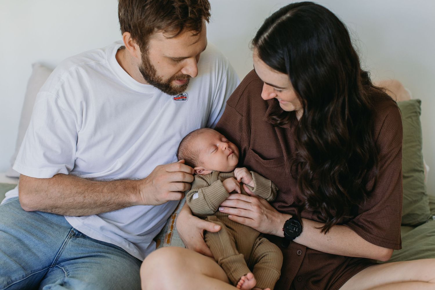 New parents smiling at their newborn baby while sitting together indoors.