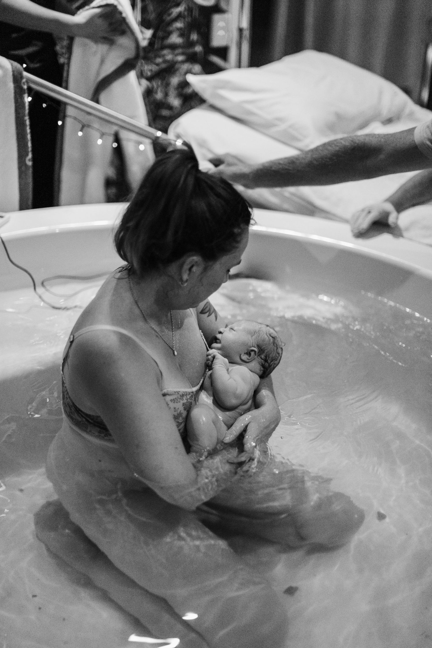 Black and white photo of a mother holding her newborn baby during a water birth in a birthing pool.