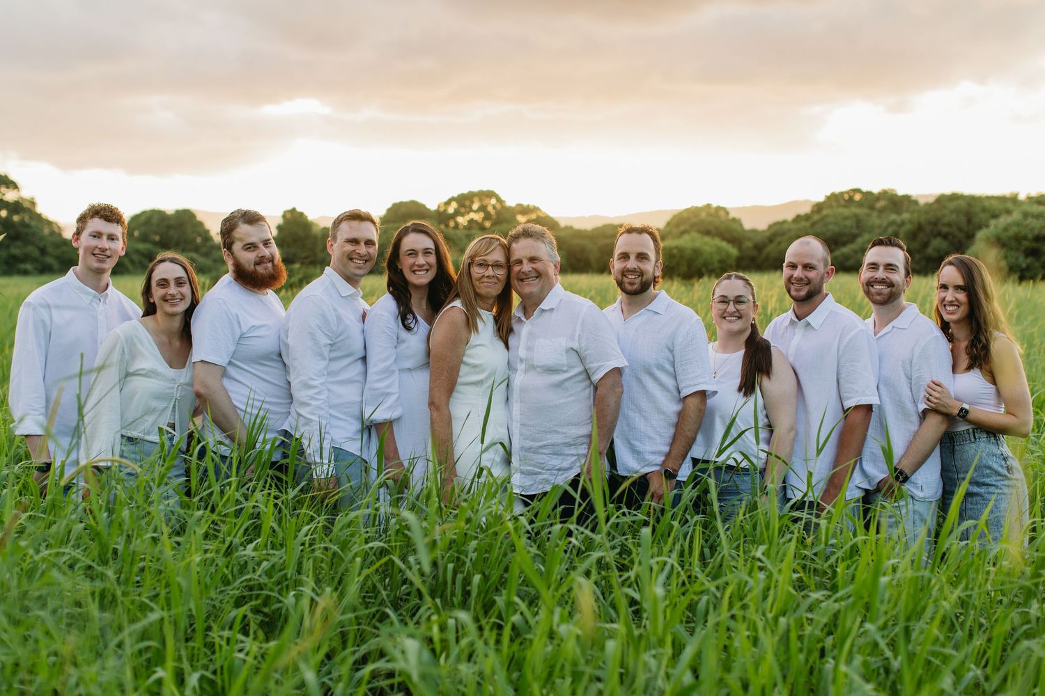 Large family group smiling together in a green field at golden hour sunset.