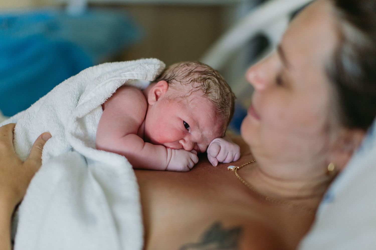 New mother gazing lovingly at her newborn baby wrapped in white towel after hospital birth.