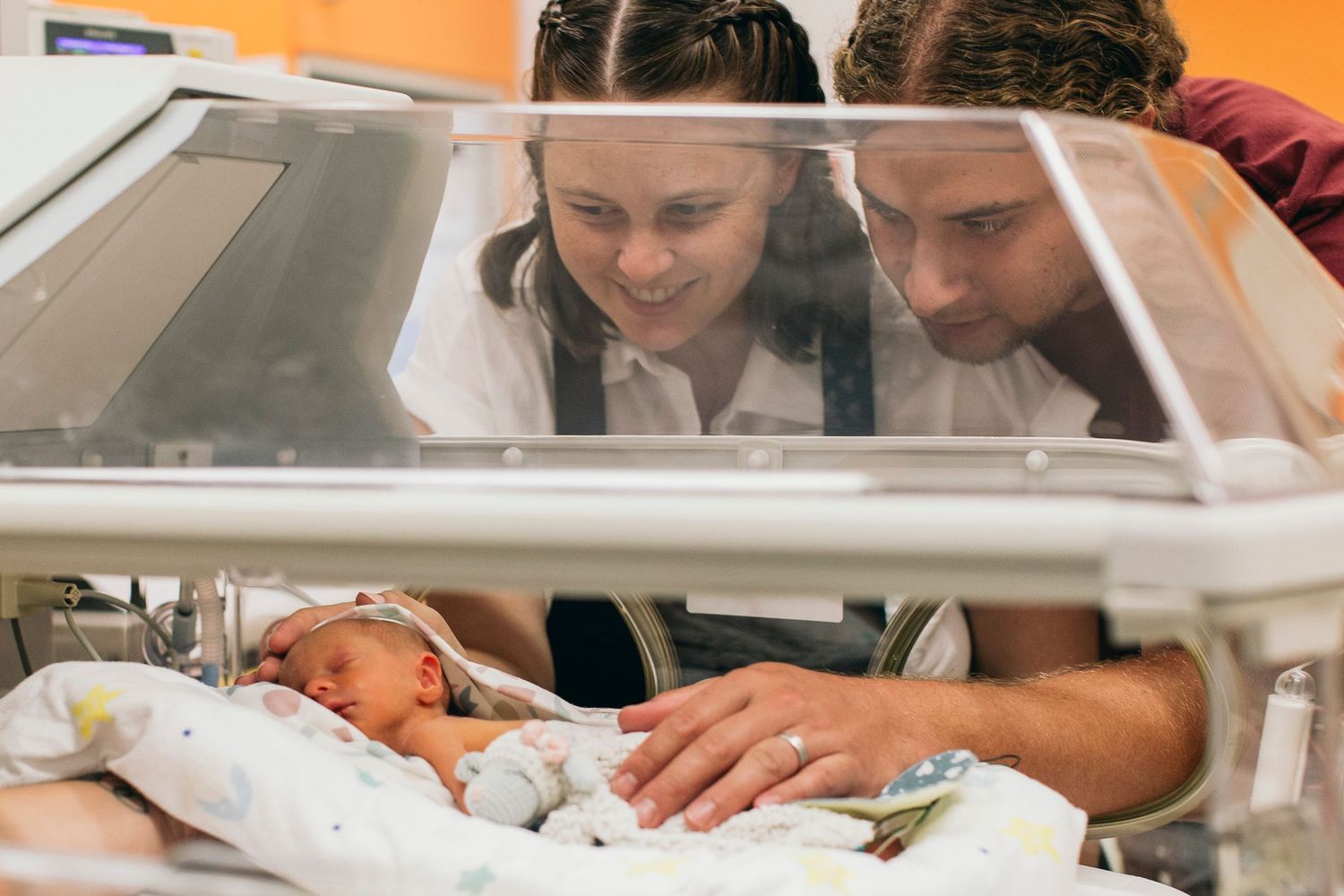 Parents lovingly gaze at their newborn baby in a hospital incubator in the neonatal intensive care unit.