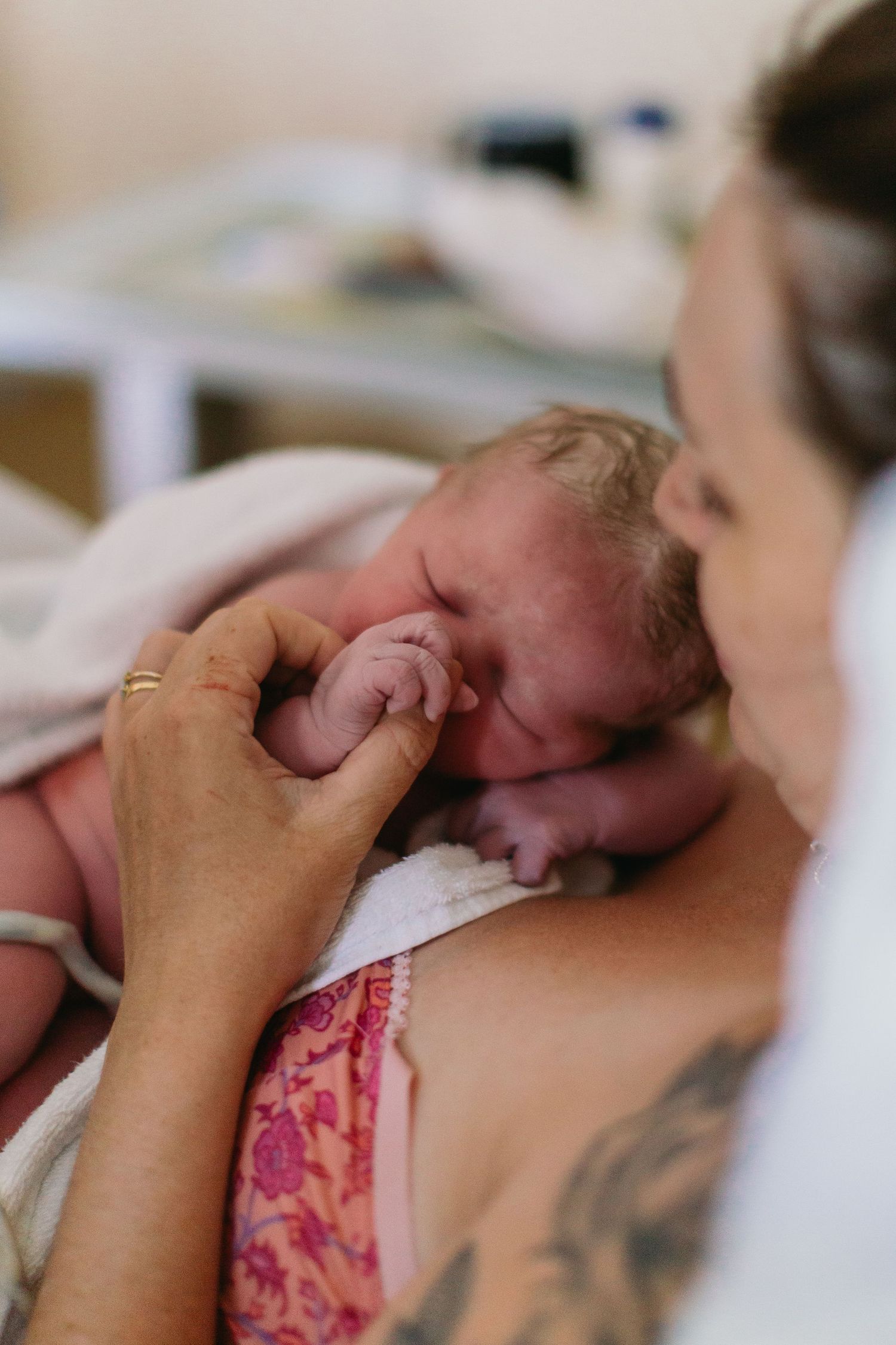 A newborn baby resting on mother's chest skin-to-skin after birth, grasping an adult's finger.