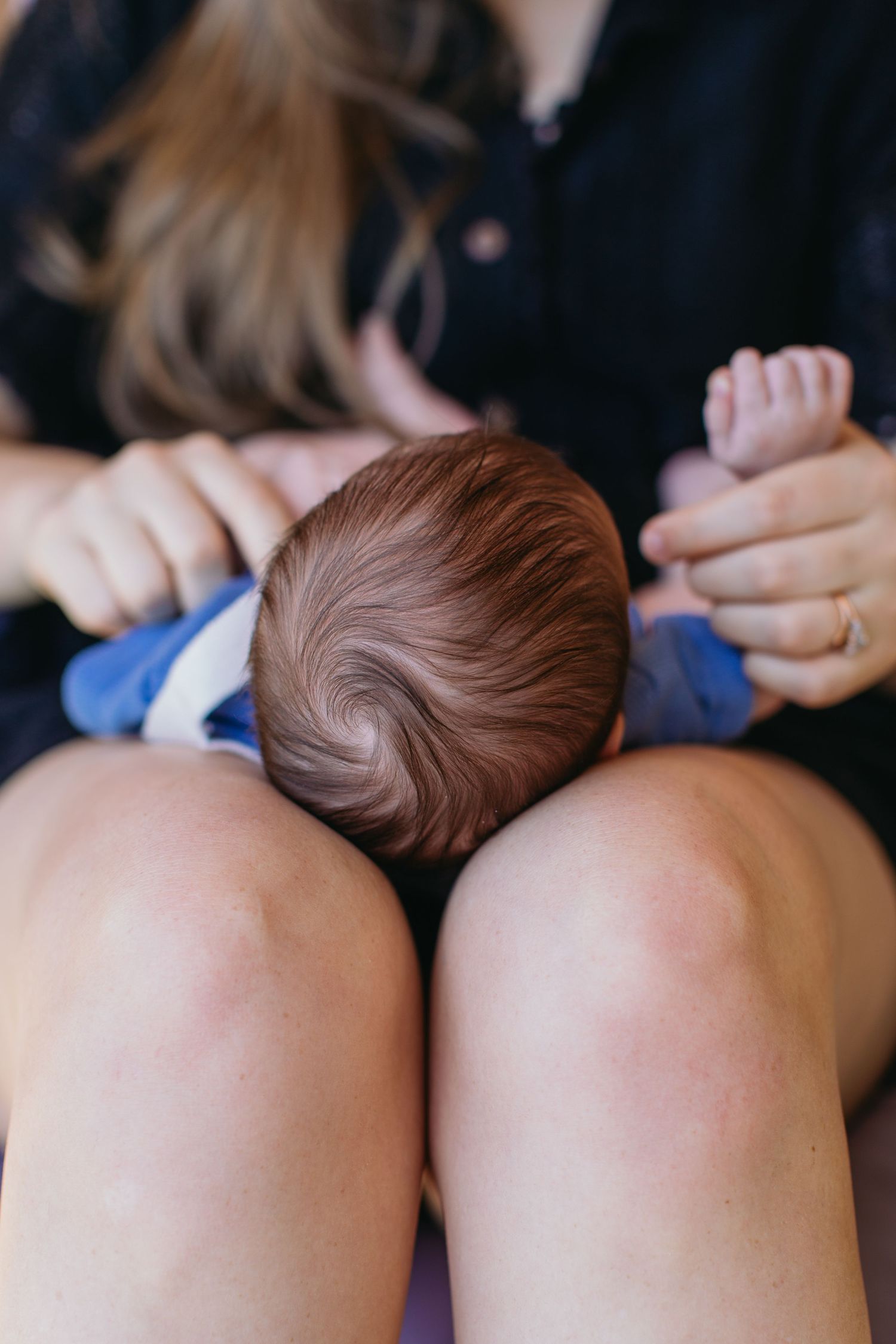 Close-up of newborn baby resting on mother's knees, showing infant's brown hair and tiny hands.