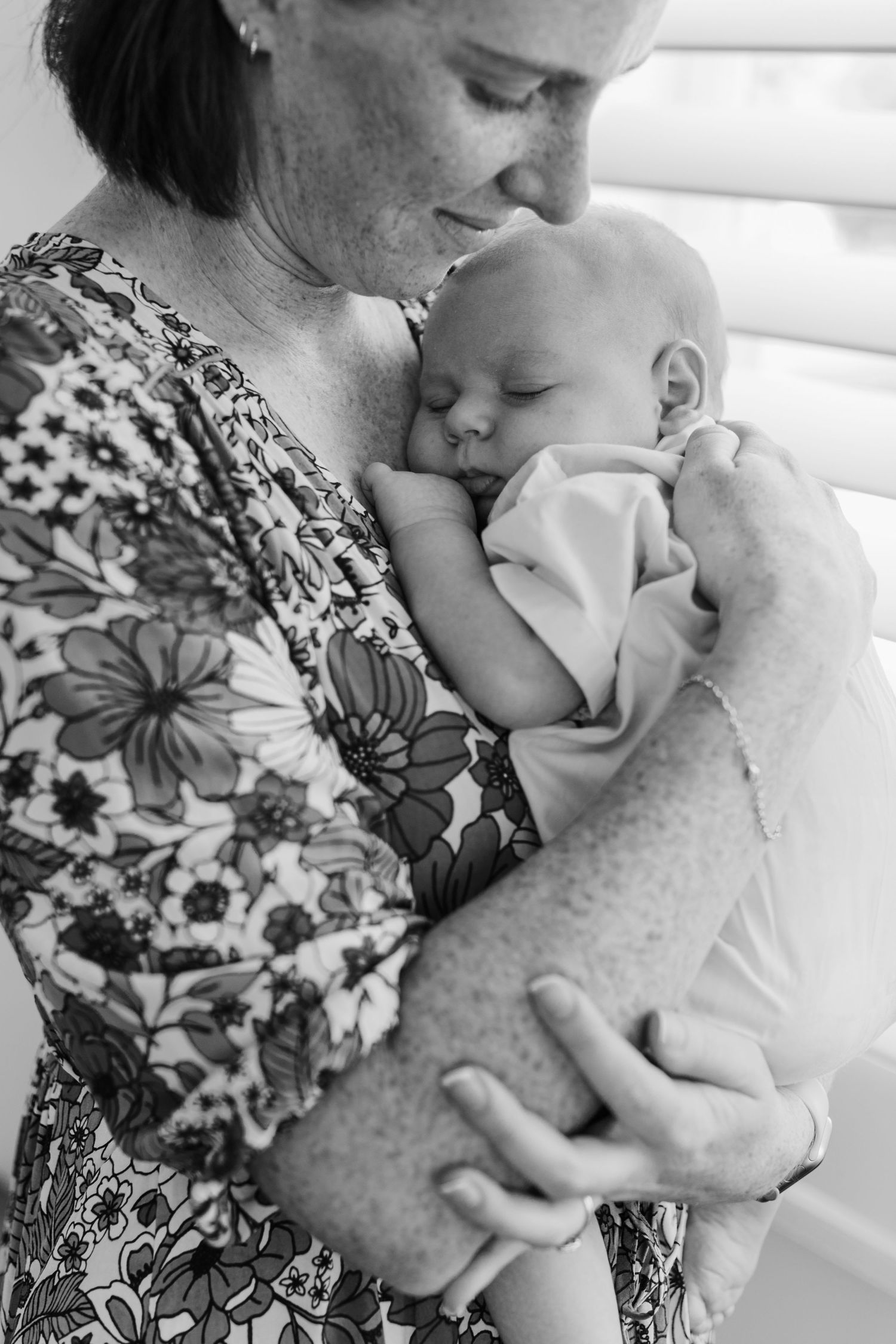 Tender black and white photo of a woman cradling a sleeping newborn baby in her arms.