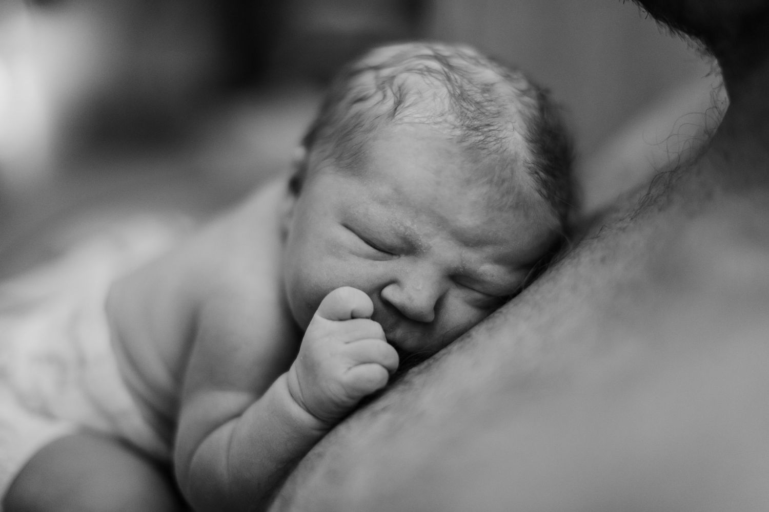 Black and white close-up of peaceful sleeping newborn baby resting on parent's chest.