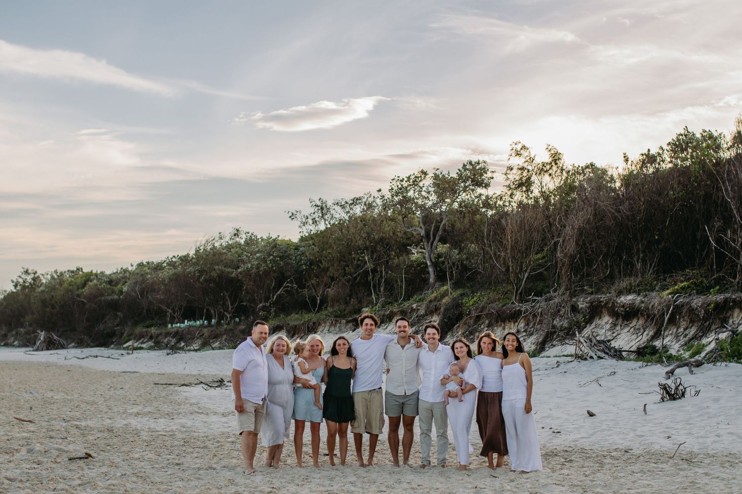 Family group portrait on sandy beach at sunset with lush green dunes backdrop.