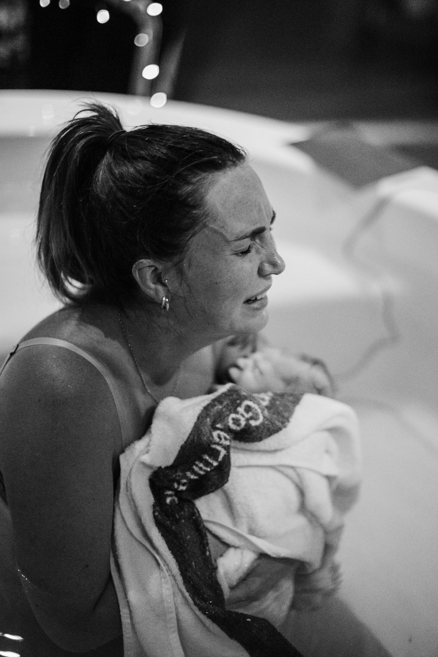 Emotional new mother holds her newborn baby wrapped in towel after water birth.