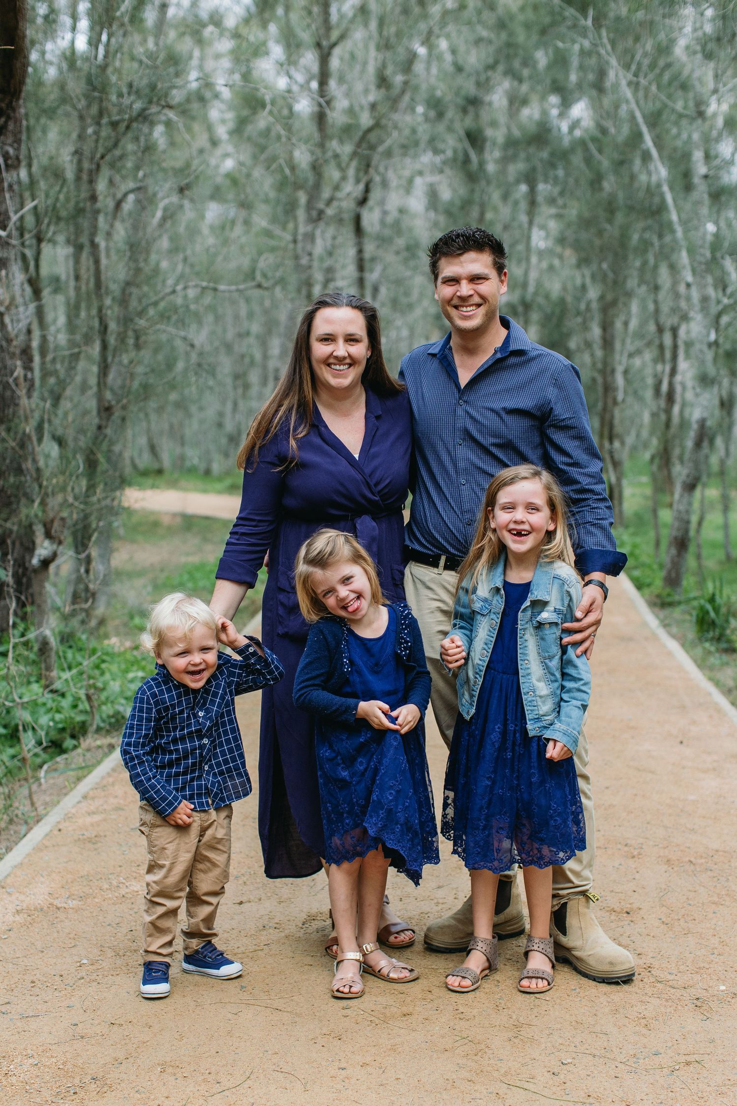Family of five posing on a path in a eucalyptus forest, wearing coordinated navy blue outfits for a portrait.