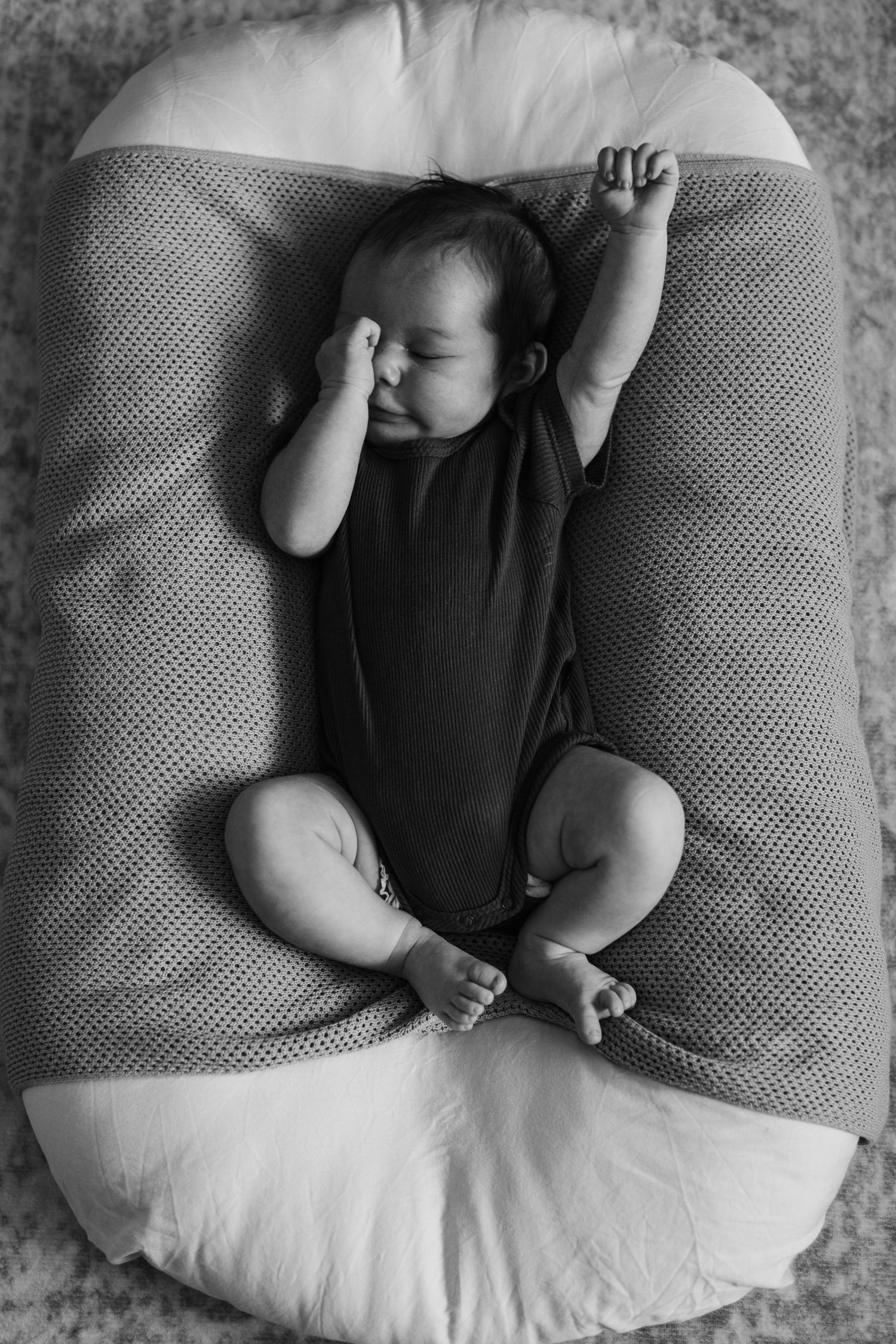 Sleeping newborn baby in black onesie lying in white nursing pillow, black and white photo.