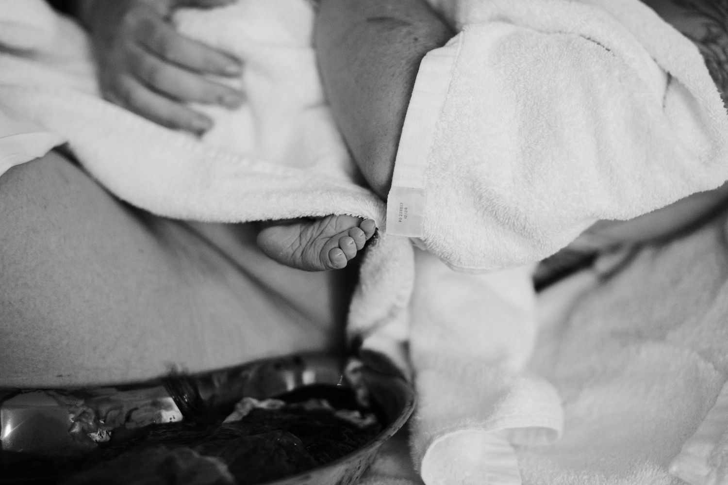 Black and white photo of a newborn baby wrapped in white towels being held after birth.