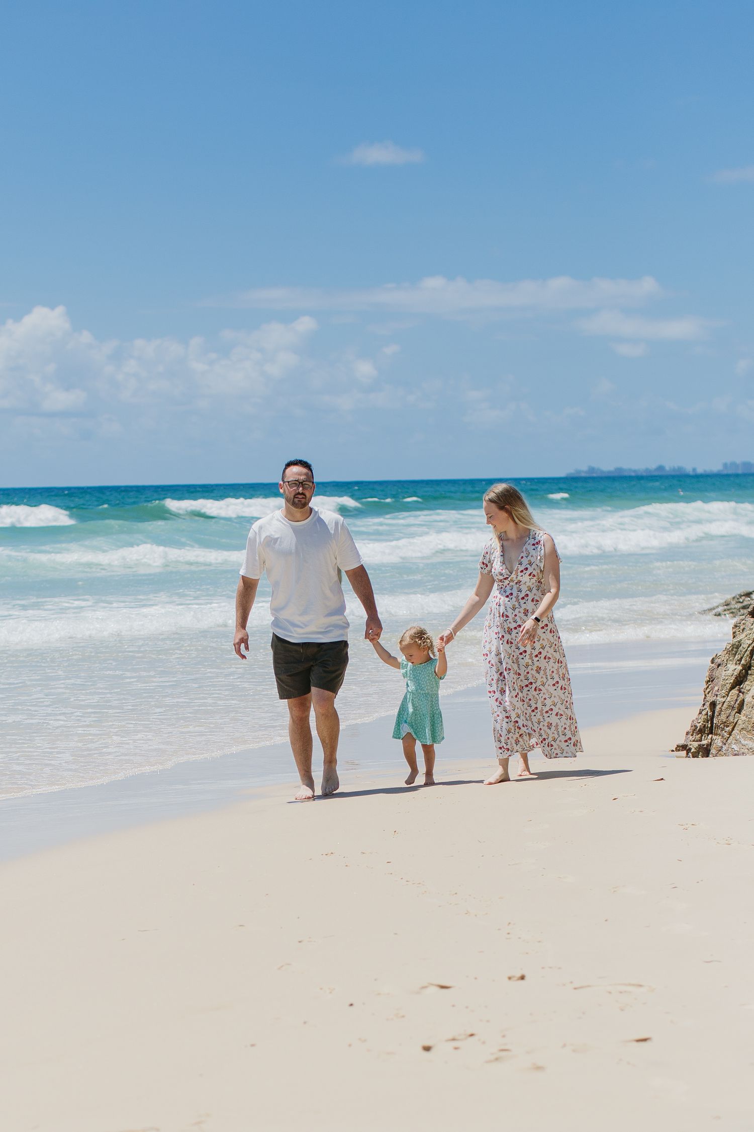 Joyful family walking hand-in-hand along a tropical white sand beach with turquoise ocean waves.