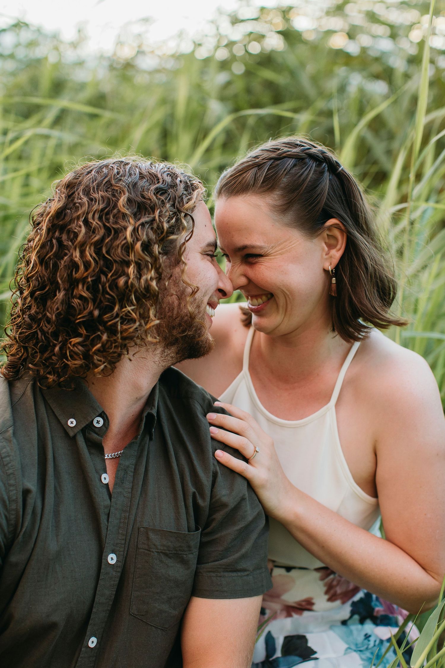 A joyful couple shares an intimate moment laughing together outdoors surrounded by lush green grass.