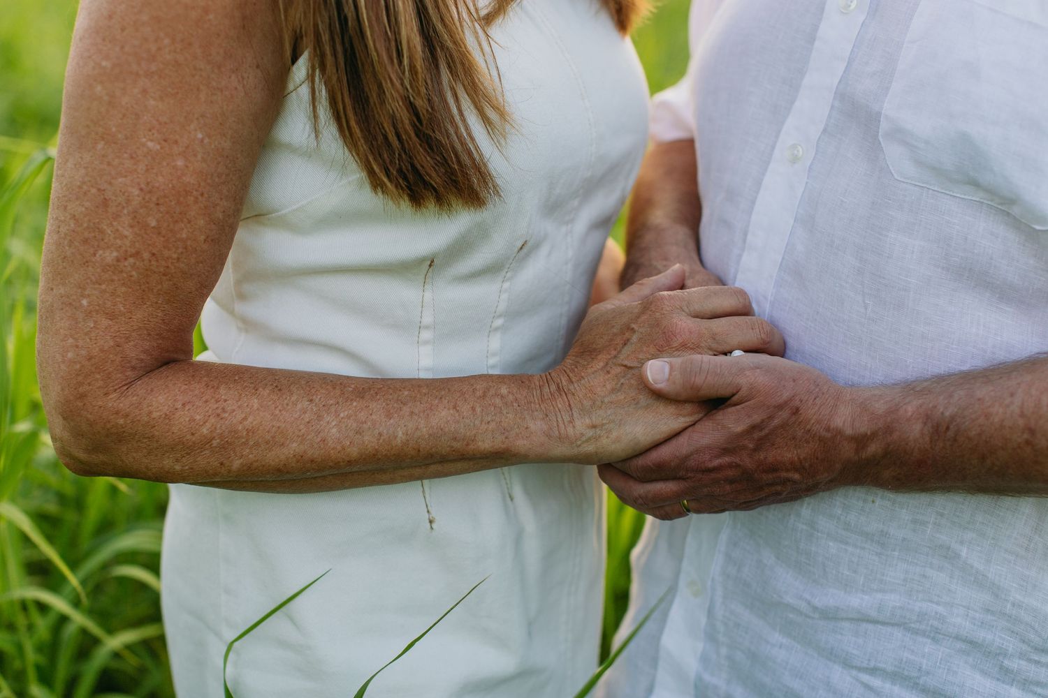 Couple in white outfits holding hands outdoors in a green field, romantic close-up photo.