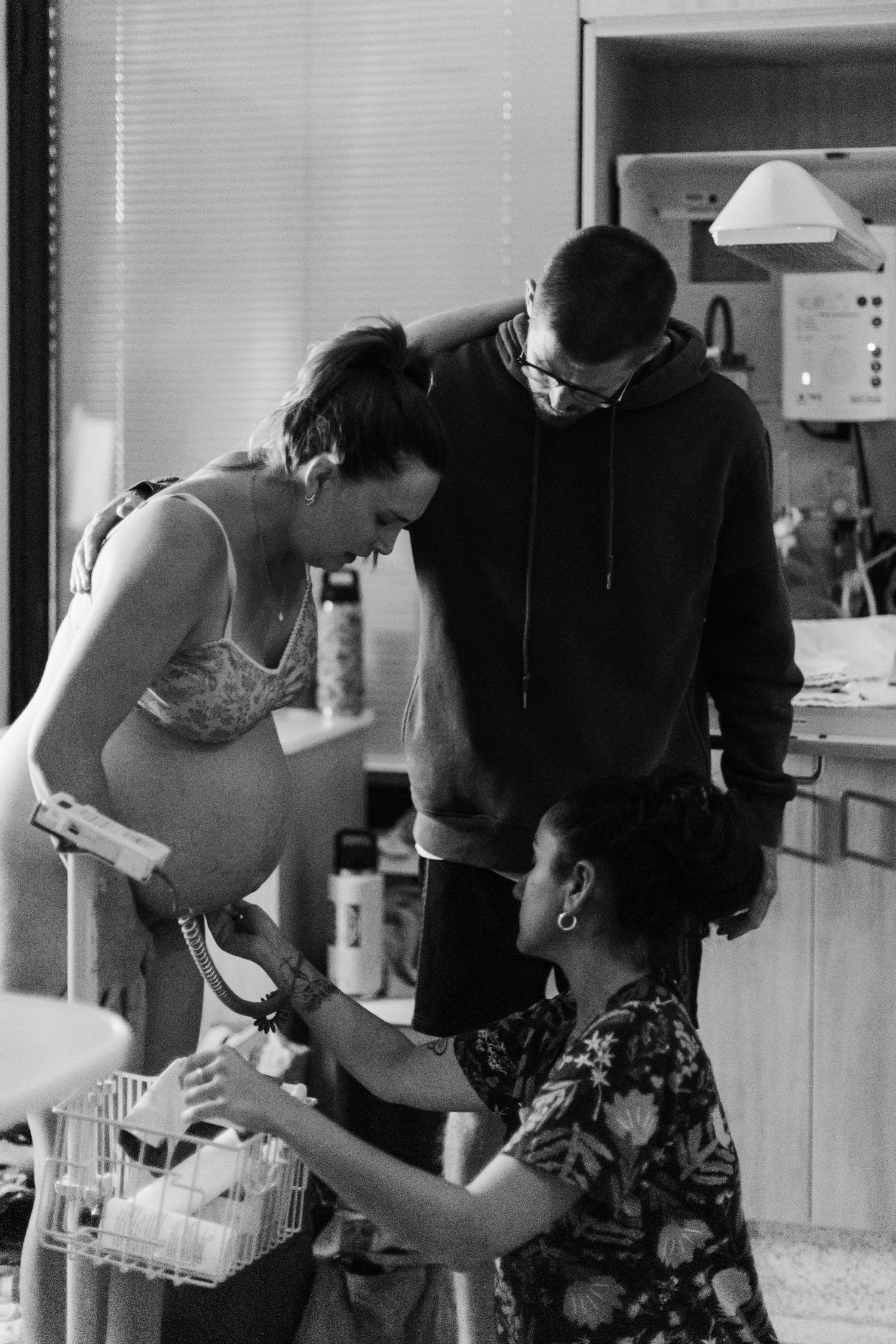 Black and white photo of pregnant woman with partner and midwife during prenatal checkup in medical setting.
