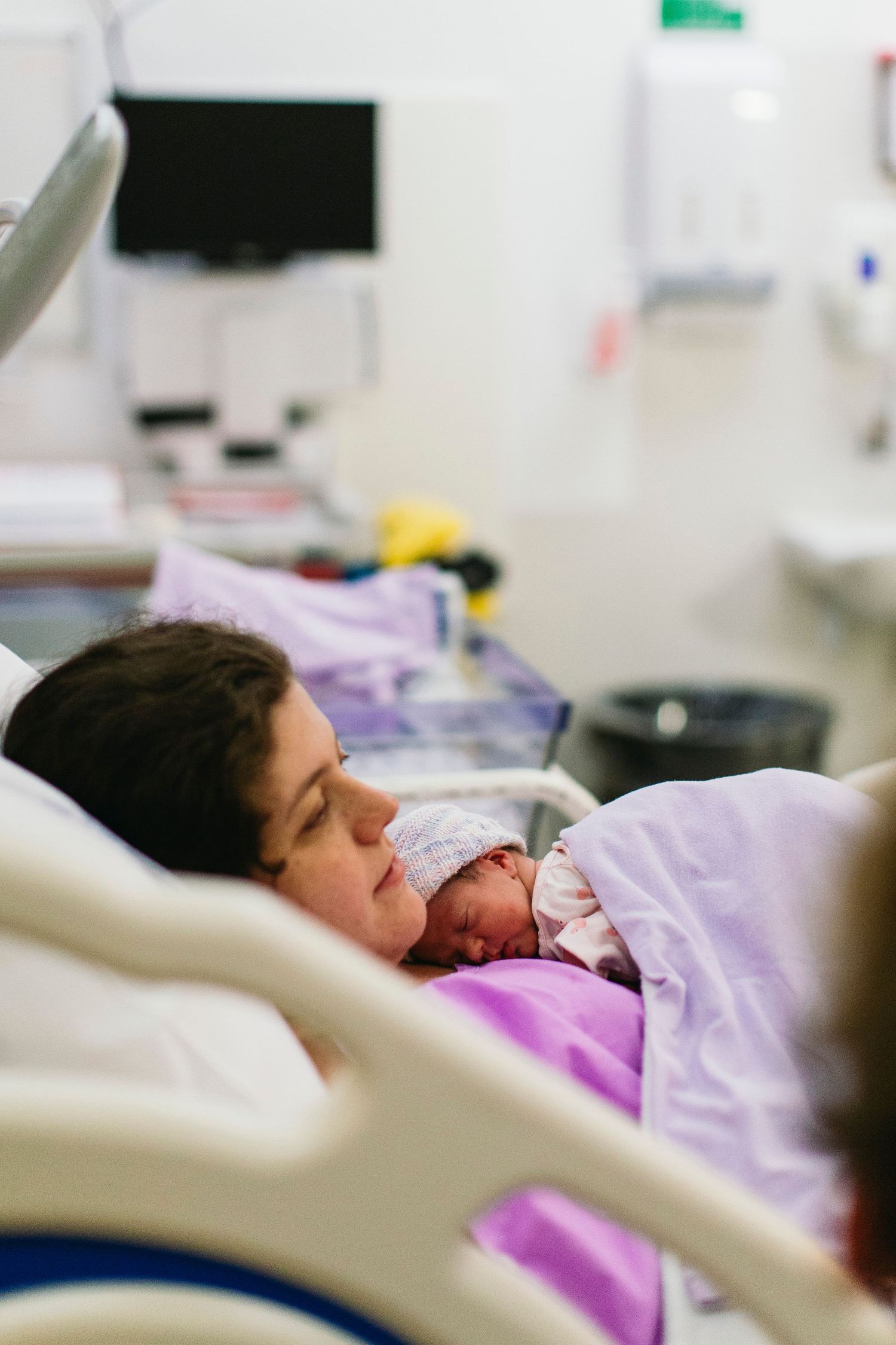 New mother lying in hospital bed holding her newborn baby skin-to-skin after delivery in maternity ward.
