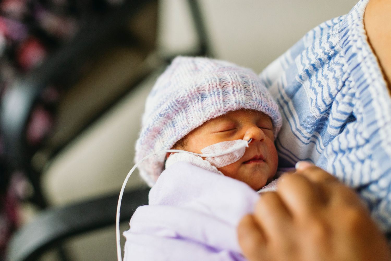 Newborn baby in NICU wearing knit hat with nasal tube, cradled in parent's arms in hospital.