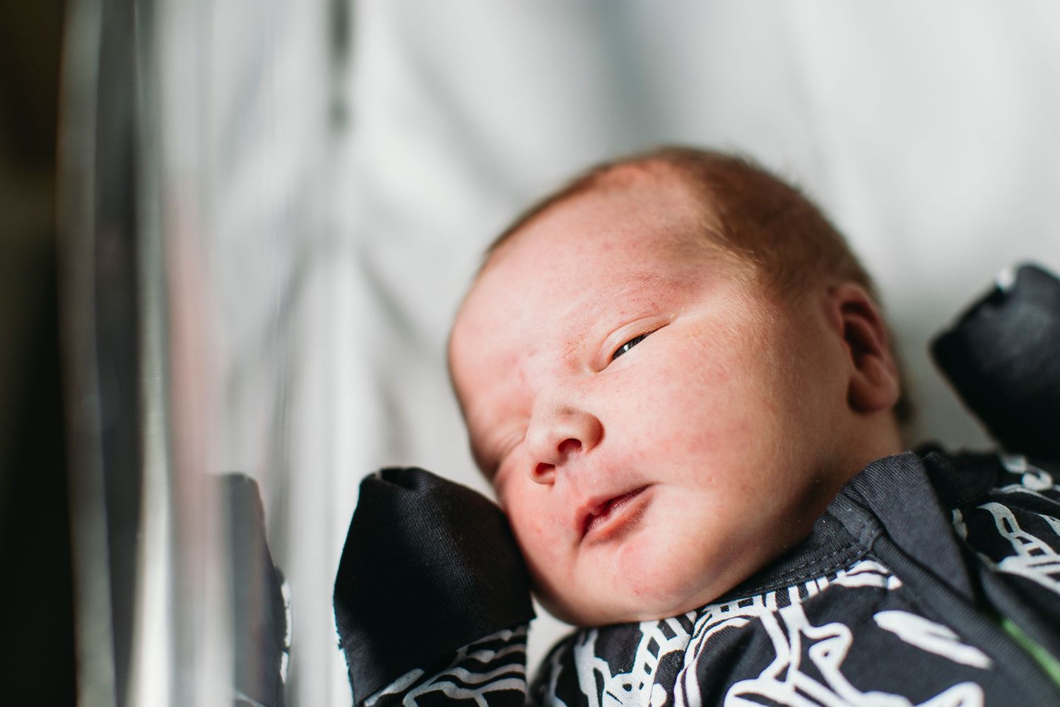 Peaceful newborn baby sleeping in a hospital bassinet wearing a black and white patterned outfit.